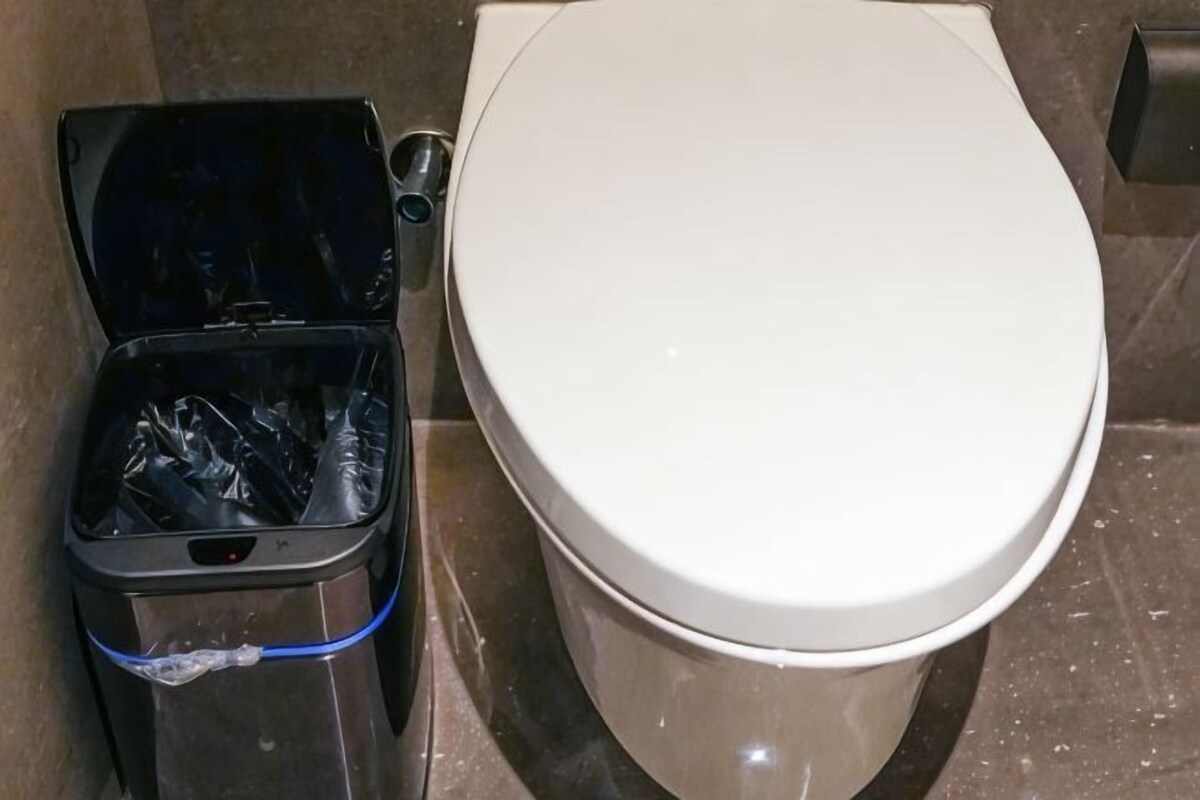 Des toilettes avec un abattant fermé et une poubelle à côté.