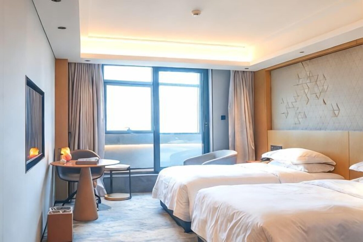 Une chambre d’hôtel avec deux lits, un bureau, une chaise et une grande fenêtre.