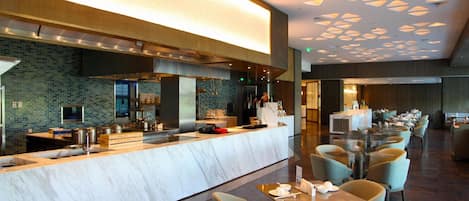 A modern restaurant with a marble counter, seating area, and a patterned ceiling.