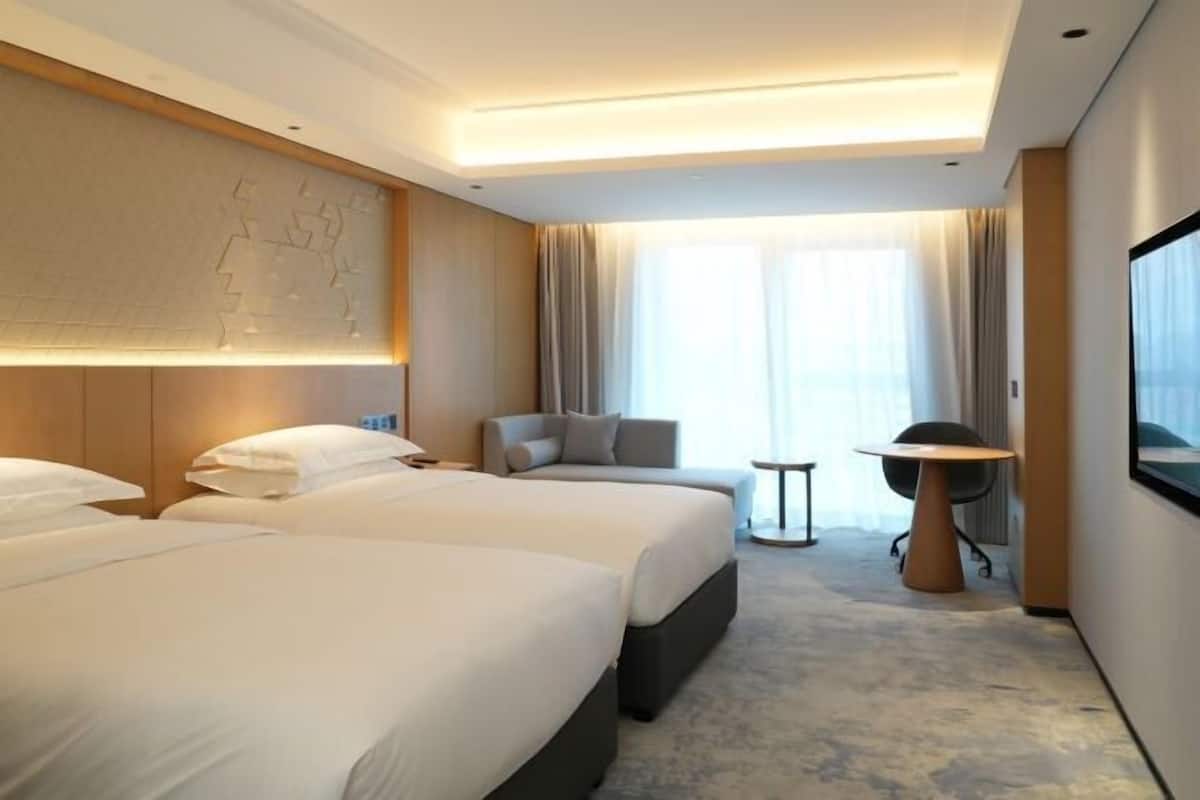 A hotel room with two beds, a seating area, a small table, and a TV.