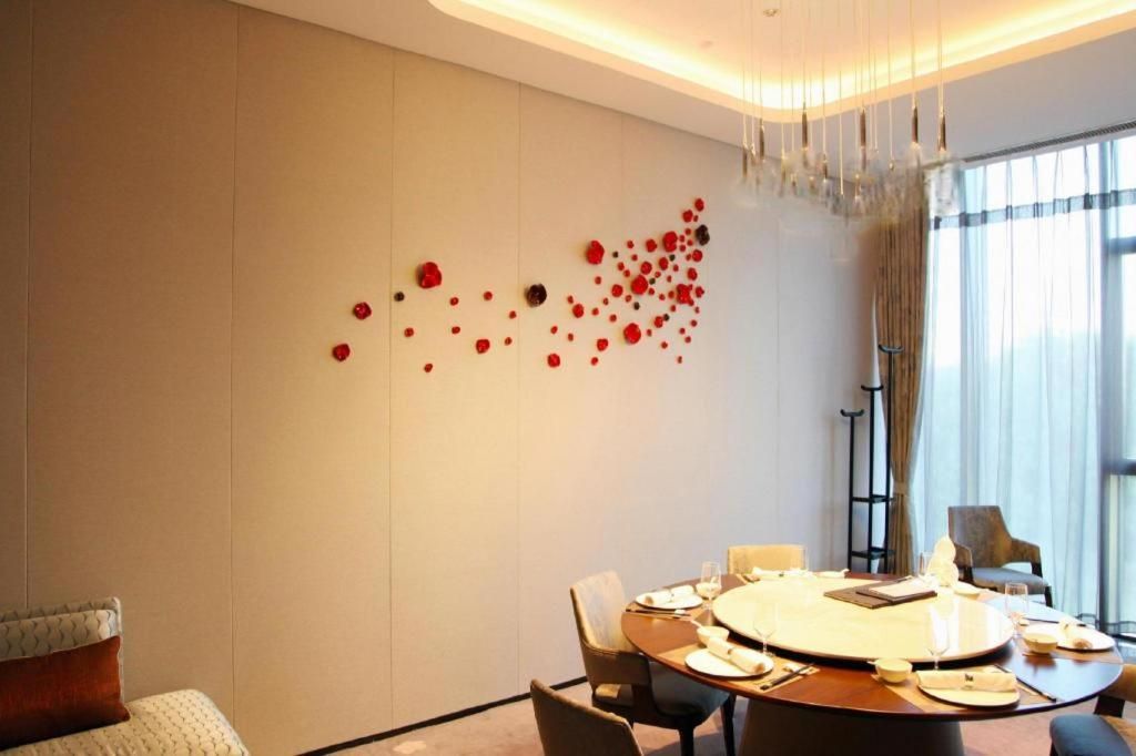 Un comedor moderno con una mesa redonda dispuesta para cuatro personas, una instalación de arte en la pared y un gran ventanal con cortinas.