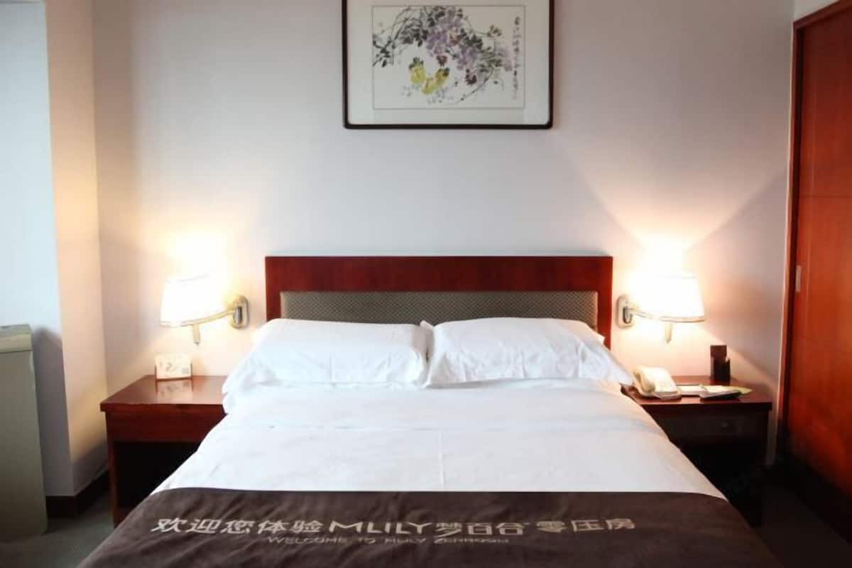 Ein Hotelzimmer mit einem ordentlich bezogenen Bett, zwei Nachttischlampen, einem Holz-Kopfteil und einem gerahmten Kunstwerk an der Wand.