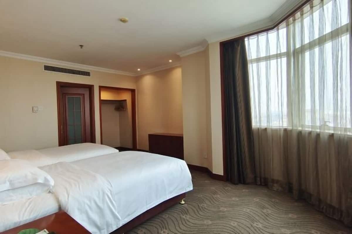 A hotel room with two beds, a large window with curtains, and a carpeted floor.