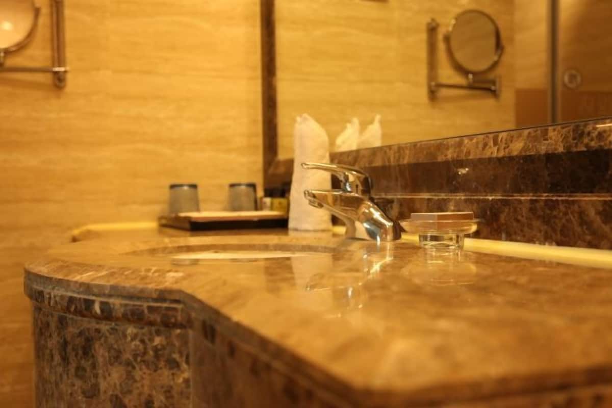 A bathroom with a marble sink, a mirror, and a towel dispenser.