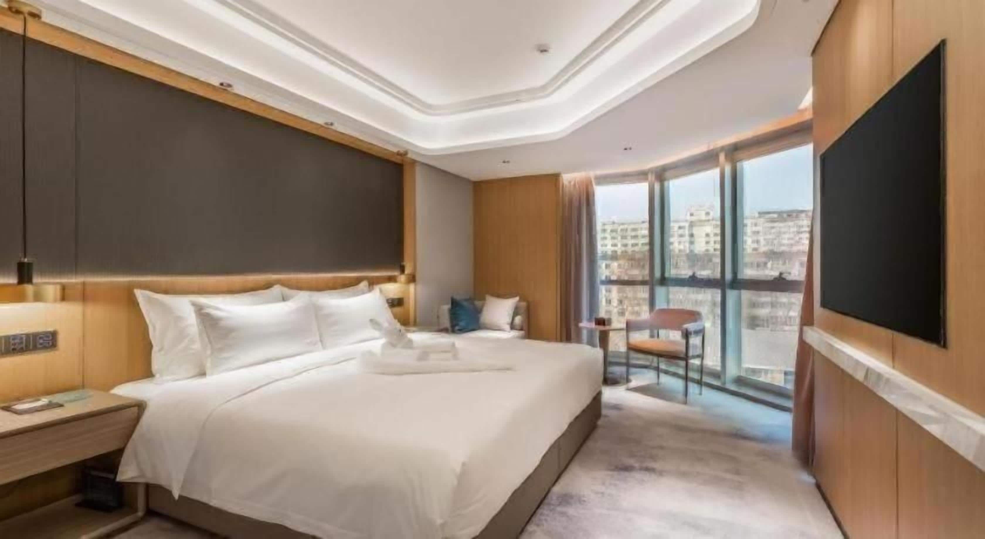 Habitación de hotel con una cama grande, un televisor de pantalla plana, un escritorio y un balcón con vistas a la ciudad.
