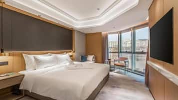 Habitación de hotel con una cama grande, un televisor de pantalla plana, un escritorio y un balcón con vistas a la ciudad.
