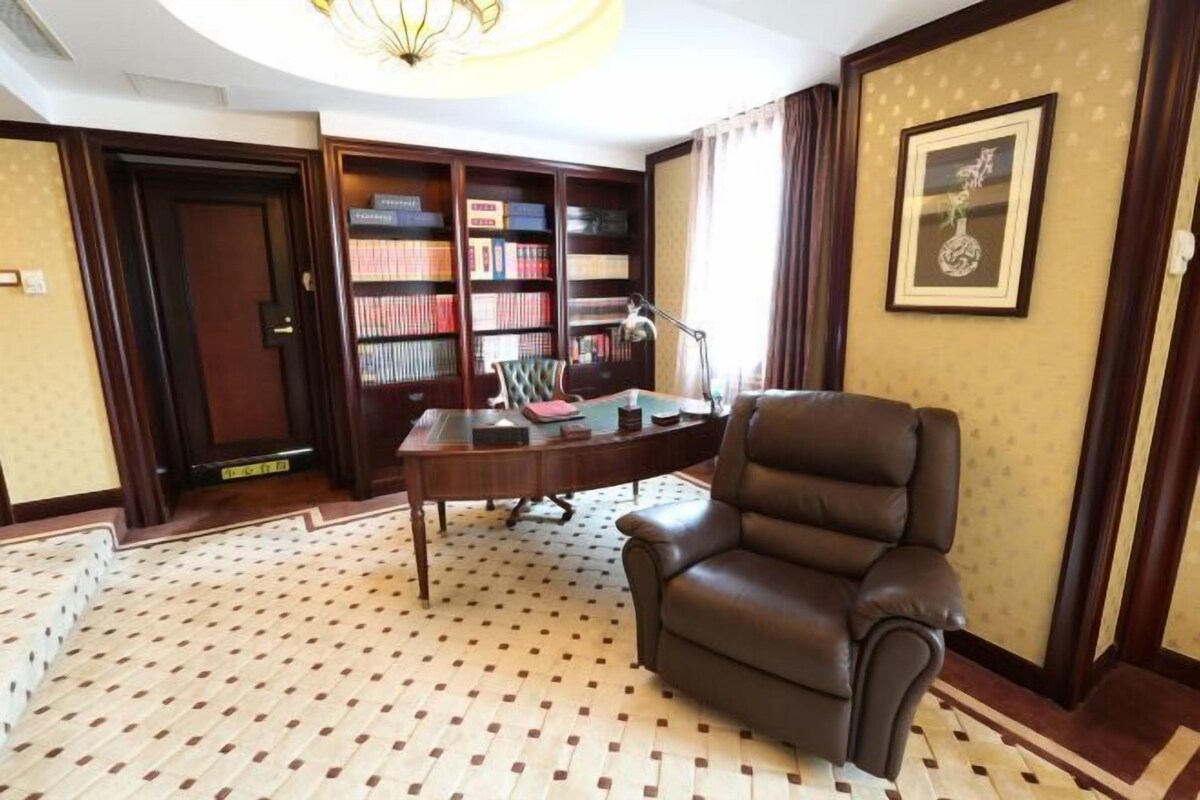 A room with a brown leather chair, a desk with a lamp, a bookshelf, and a framed picture on the wall.