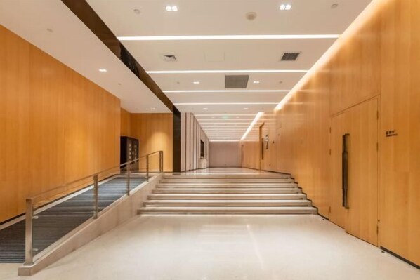 Un couloir d’hôtel moderne avec des murs en bois, une rambarde en verre et un escalier menant à l’étage supérieur.