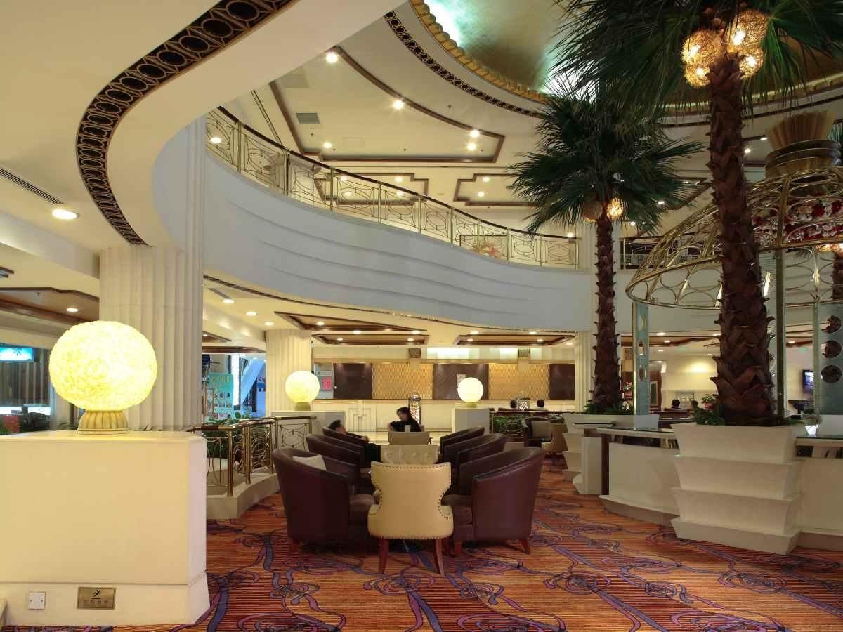 Um saguão de hotel com teto curvo, balcão de recepção, área de estar e escadaria que leva a um andar superior.
