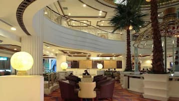 Um saguão de hotel com teto curvo, balcão de recepção, área de estar e escadaria que leva a um andar superior.