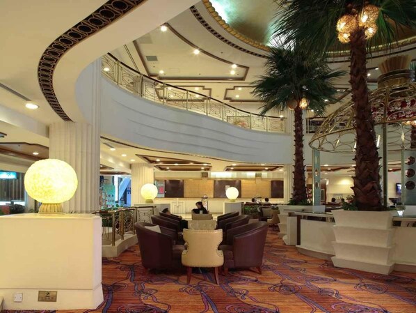 A hotel lobby with a curved ceiling, a reception desk, seating area, and a staircase leading to an upper level.