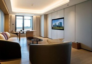 A modern hotel room with a sofa, a small table, a TV mounted on the wall, and a large window providing a view of the city. - RoyalRae YongXing Garden Hotel (Beijing)