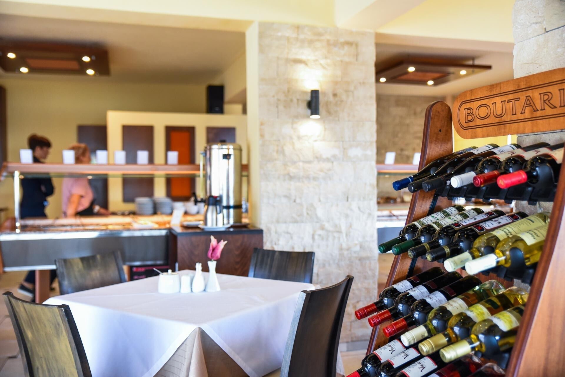 Interior de un restaurante con una estantería de vinos que dice "BOUTARIS" y una máquina de café.