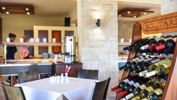 Interior de un restaurante con una estantería de vinos que dice "BOUTARIS" y una máquina de café.