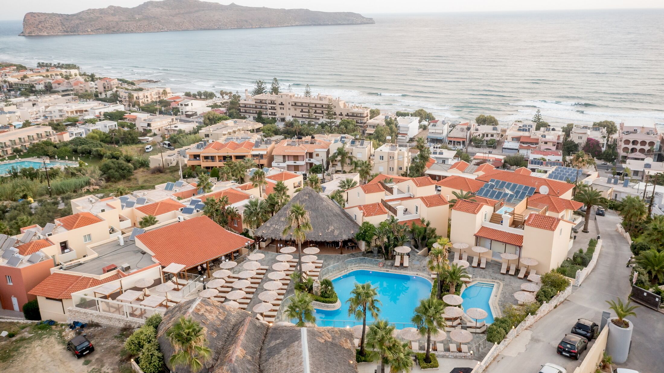 Un resort costiero con diverse piscine, tra cui una piscina centrale con tetto di paglia, e vista sul mare.