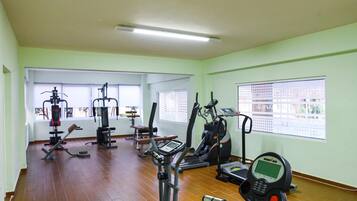 A gym with various exercise machines, large windows, and a tiled floor.