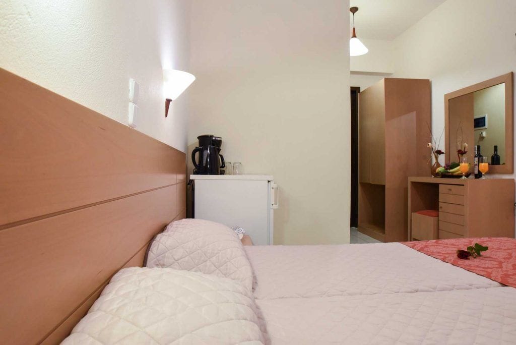 A hotel room with a bed, a small desk with a coffee maker, a mirror, and a dresser.