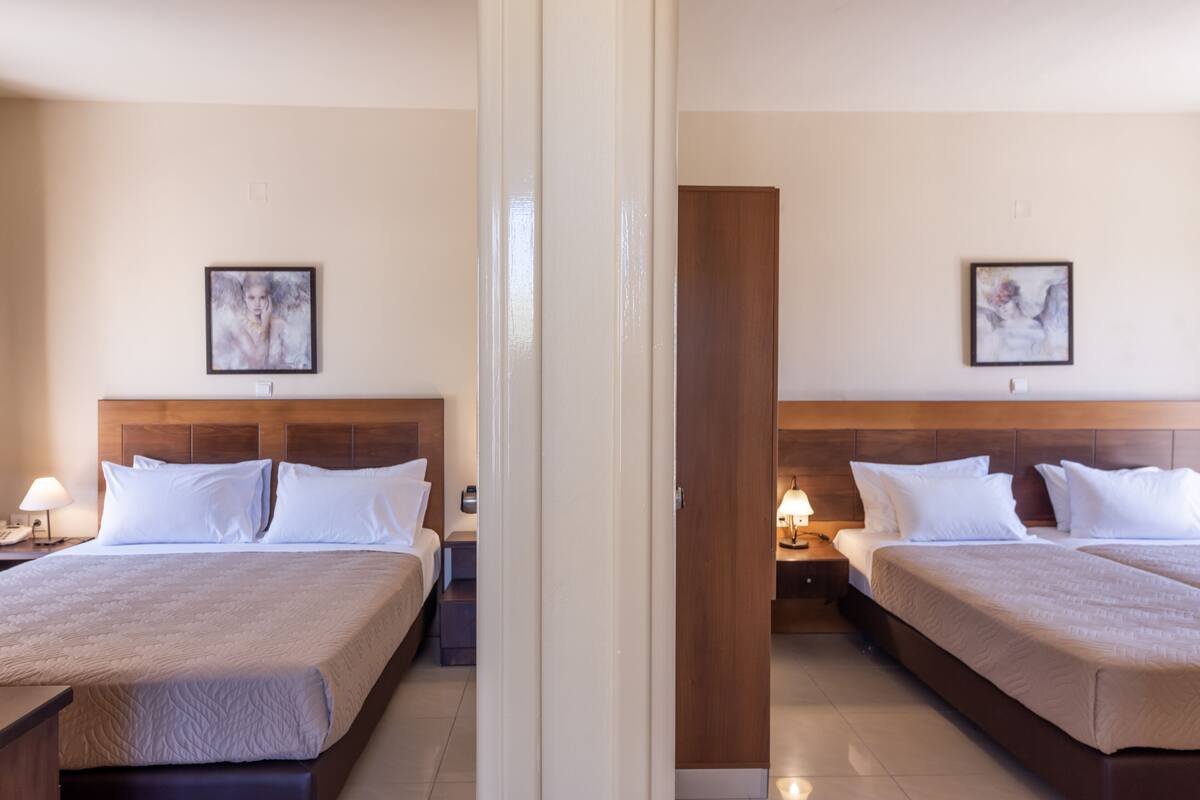 Hotellihuone, jossa on kaksi sänkyä. Jokaisessa sängyssä on puinen pääty, valkoiset vuodevaatteet ja seinällä on kehystetty kuva.