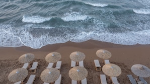 A beach with rows of sun loungers and thatched umbrellas. - Eurohotel Theo Hotel (Chania)