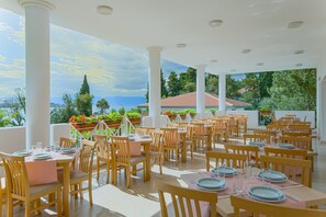 Un restaurante con mesas dispuestas para comer, columnas blancas y vista al mar.