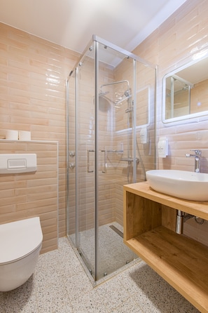 Un bany modern amb dutxa d'estuc de vidre, un lavabo blanc i un vàter.