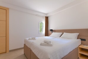 Una habitación de hotel con cama, mesita de noche, lámpara de pared y ventana con cortinas.
