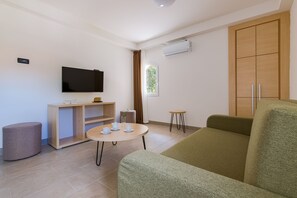 A modern living room with a flat-screen TV, a wooden cabinet, a round coffee table, a green sofa, a small stool, and a window with curtains.