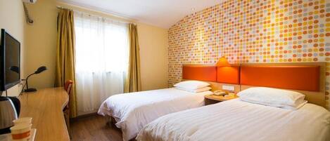 A hotel room with two beds, a desk with a computer, and a wall with a polka dot pattern.