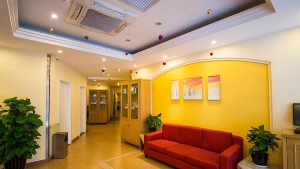 A hotel lobby with a red sofa, potted plants, and framed artwork on the wall. - Home Inn Jinsong (BEIJING)