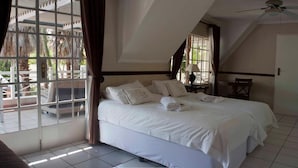 Een slaapkamer met een groot bed, een plafondventilator en uitzicht op de omgeving door een raam.