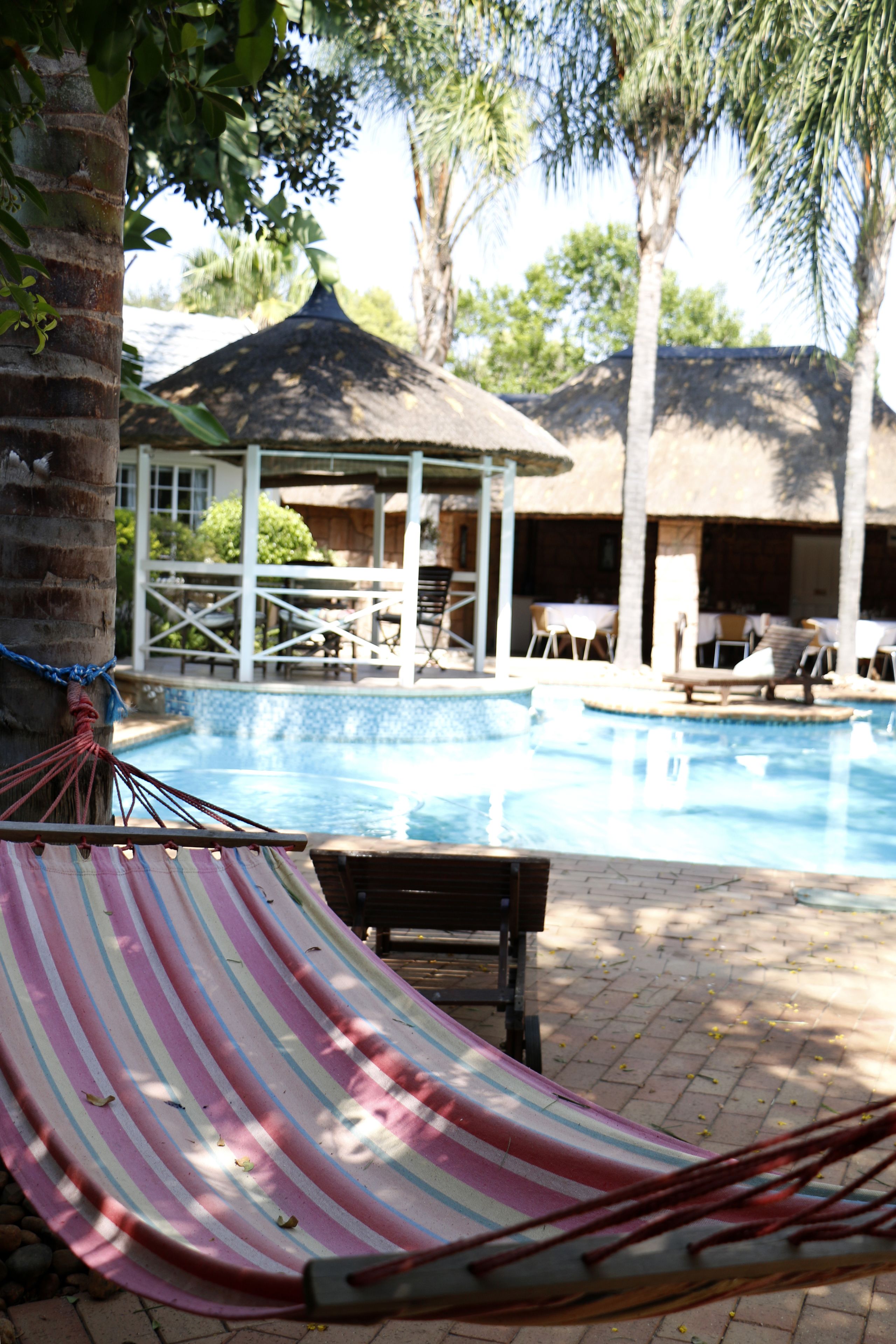 Zona de piscina con una hamaca, sillones reclinables y un pabellón.