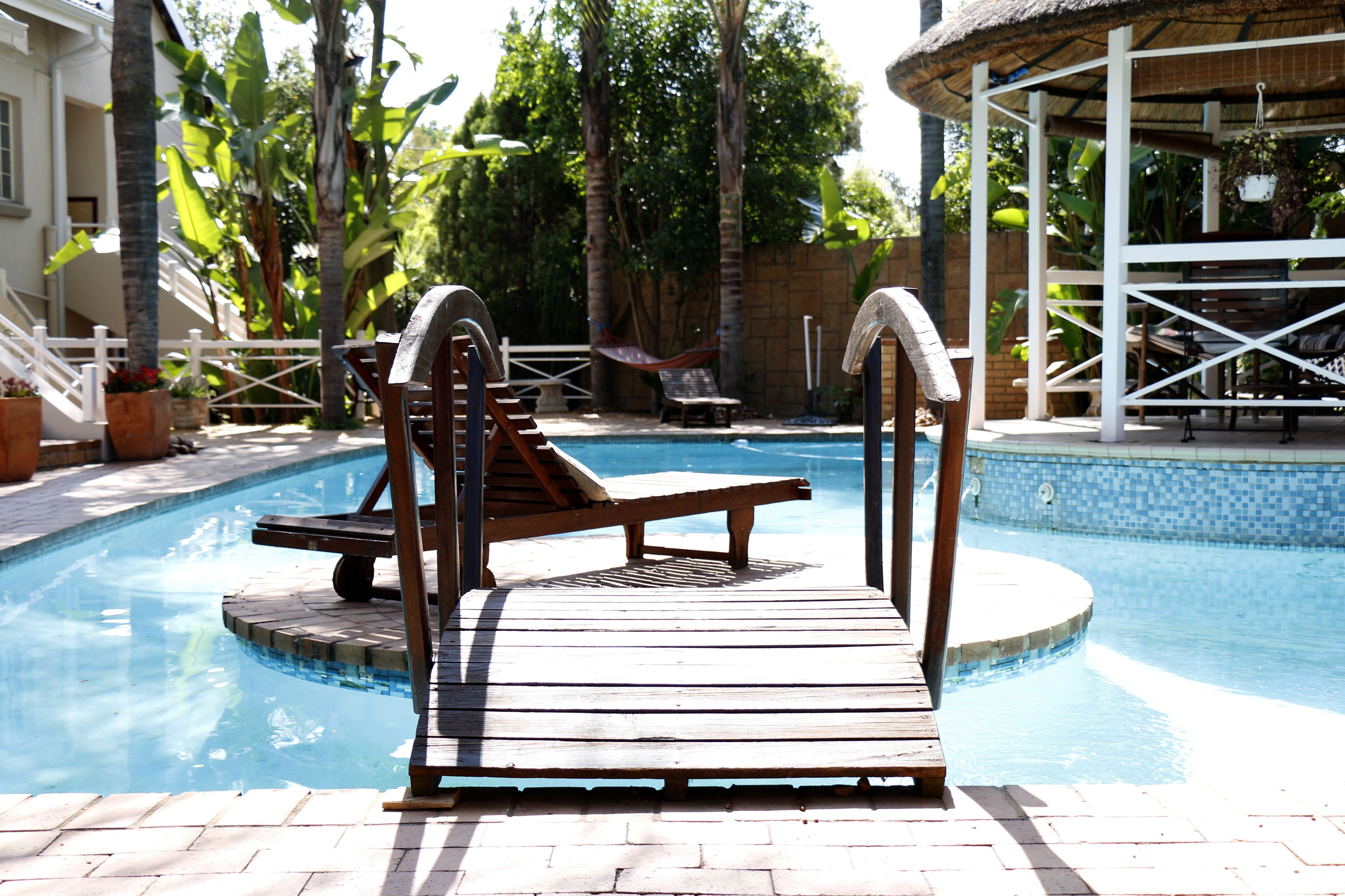 A pool area with a wooden deck, lounge chairs, and a thatched-roof structure.