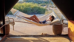 Una hamaca en una terraza de madera con vista a una playa y vegetación.