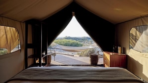 Una tienda de campaña con una cama, un escritorio de madera y vistas a la playa y las dunas.
