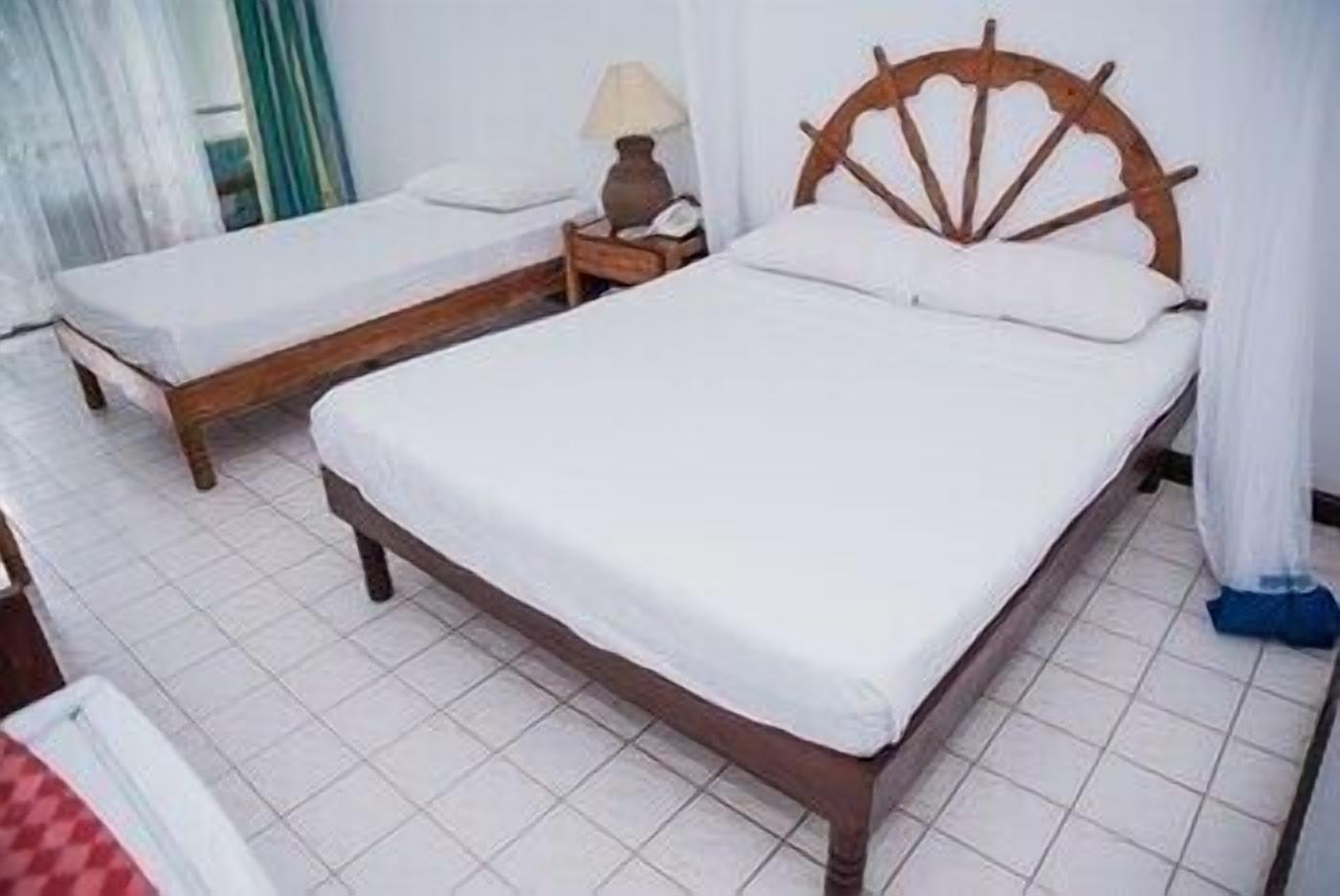 A double bed with a wooden headboard, a bedside table with a lamp, and a small table with a red and white checkered tablecloth.
