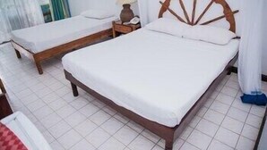 Ein Doppelbett mit Holz Kopfteil, ein Nachttisch mit Lampe sowie ein kleiner Tisch mit rot-weißer Karodecke.