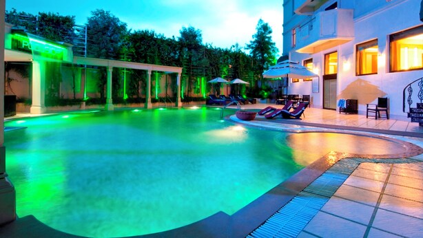 A swimming pool with lounge chairs and umbrellas, surrounded by a building with multiple floors and balconies. - Howard Plaza The Fern, Agra (Agra)