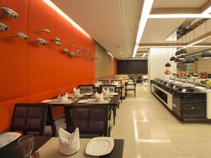A restaurant with a modern interior, featuring orange walls, black and white furniture, and a buffet area. - Howard Plaza The Fern, Agra (Agra)