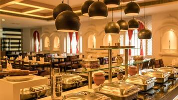 Un espace buffet doté de plusieurs points de service pour les aliments, de luminaires suspendus et d’un coin salon avec des tables et des chaises.