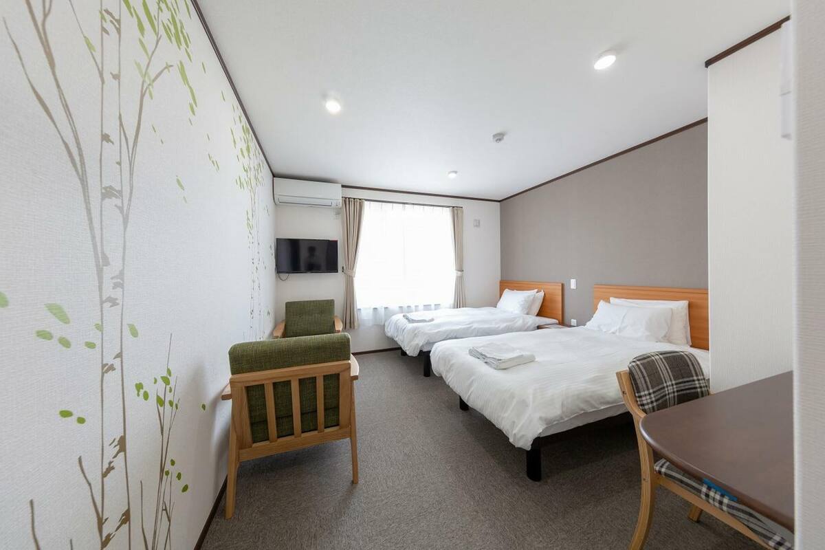 A hotel room with two beds, a desk, a chair, a TV, and a window with curtains.