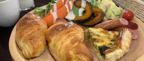 A wooden plate with croissants, a quiche, grilled vegetables, and a side salad.