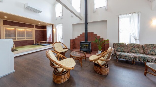 A spacious living room with a fireplace, wicker furniture, and a sofa. - Pension Lavender (Furano)