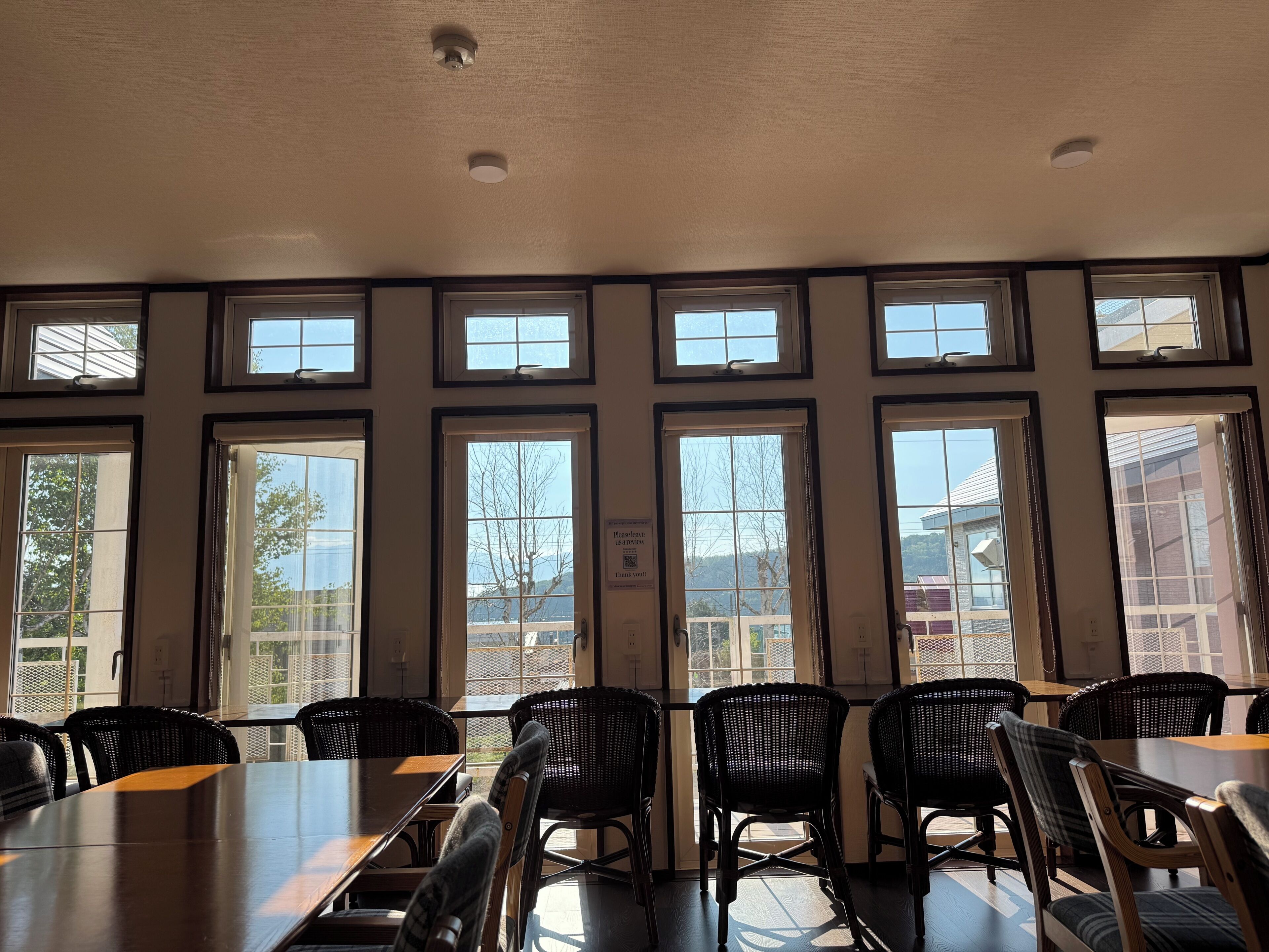 A conference room with a long table and multiple chairs, large windows with blinds, and a ceiling with recessed lighting.