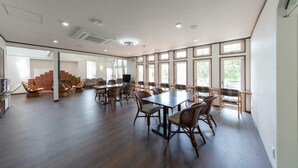 A spacious room with a large dining table, multiple chairs, and a staircase leading to an upper level. - Pension Lavender (Furano)