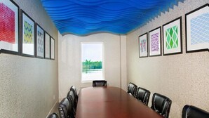 A conference room with a long table and leather chairs, framed artwork on the walls, and a window with a view of greenery. - LMI Gulf Coast Homes, Port Charlotte (Port Charlotte)