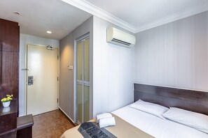 A hotel room with a bed, a desk, an air conditioning unit, a door, and a small plant.