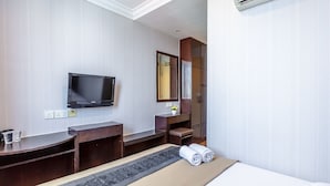 A hotel room with a bed, a desk, a television, a mirror, and an air conditioning unit.