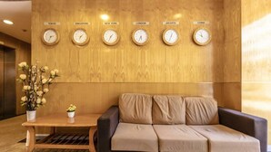 A lobby with a wooden wall, a sofa, a small table with flowers, and clocks displaying times for Tokyo, Singapore, New York, London, Jakarta, and China.