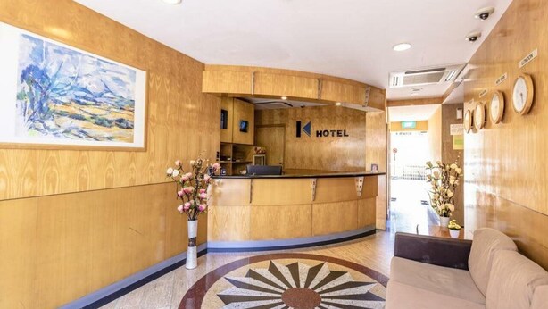 A hotel reception area with a wooden reception desk, a painting on the wall, and a clock on the wall.
