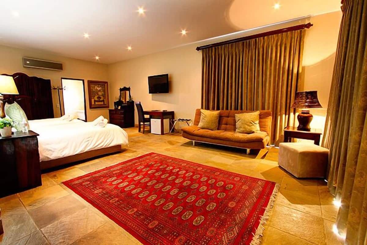 Une chambre d’hôtel avec un lit, un canapé, une télévision, un bureau et une moquette rouge.